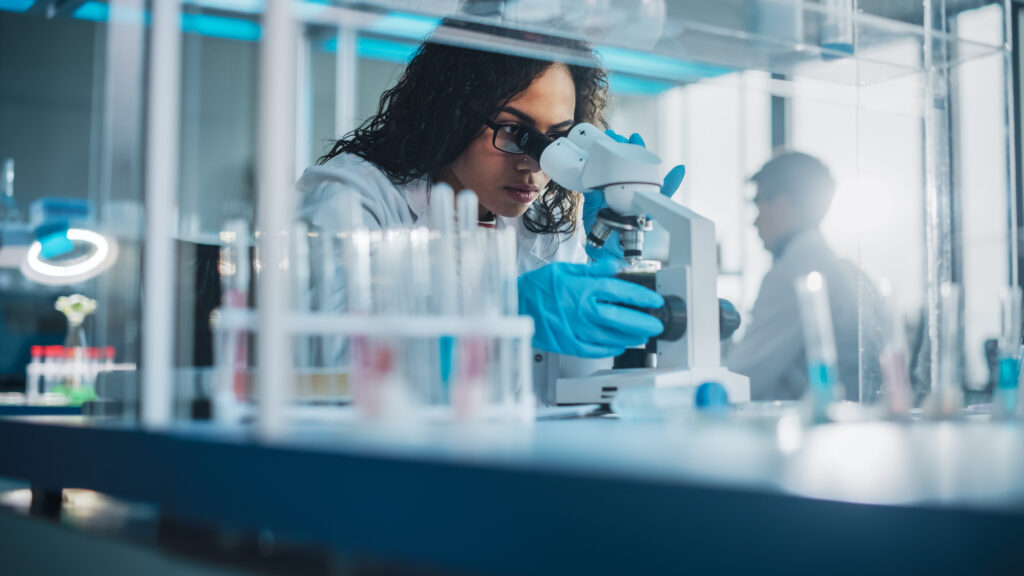A woman in a lab coat looks into a microscope in a science lab.
