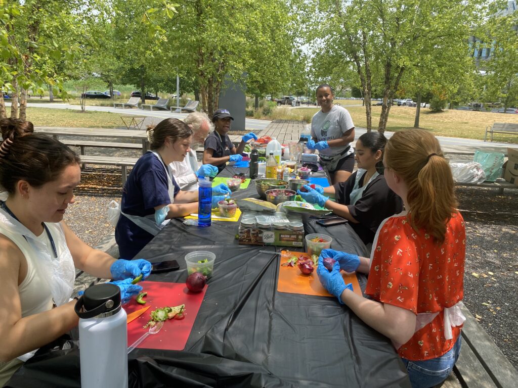 A group of adults work with vegetables on a table outdoors.