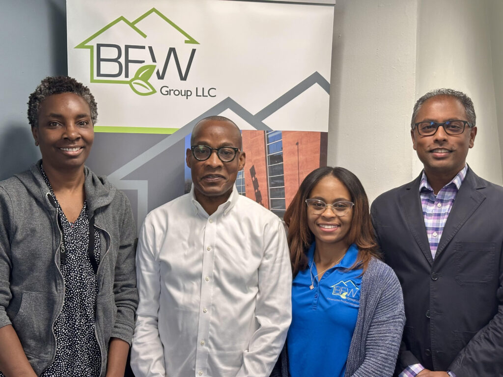 Four adults in professional wear stand in front of a BFW branded sign.