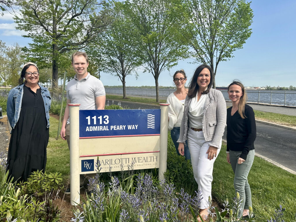 The Barilotti team stands outside on Admiral Peary Way next to their business sign.